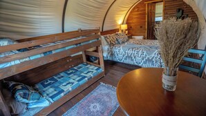 Una carpa acogedora con una cama litera, una mesita con un florero y una puerta de madera que da a un baño.