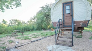 Une structure en bois couverte, dotée d’une porte et d’une échelle permettant d’y accéder, entourée d’une zone recouverte de gravier, avec une table de pique-nique et un banc.