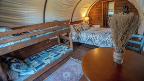 Une tente confortable avec un lit superposé, une petite table ornée d’un vase et une porte en bois donnant sur une salle de bain.
