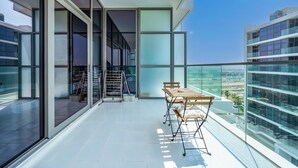 A modern balcony with a glass railing, a wooden table with chairs, and a view of a cityscape. - Luxury StayCation - Studio in Damac Hills with Balcony and Golf Views (Dubai)