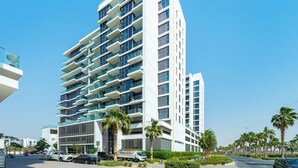 A modern multi-story hotel with balconies, a parking area, and palm trees. - Luxury StayCation - Studio in Damac Hills with Balcony and Golf Views (Dubai)