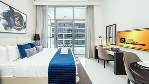 A modern hotel room with a large bed, a desk, and a view of the city through floor-to-ceiling windows. - Luxury StayCation - Studio in Damac Hills with Balcony and Golf Views (Dubai)