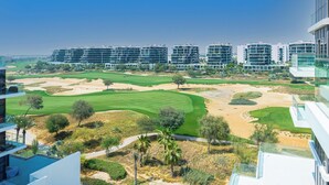 A modern building with multiple floors and large windows, overlooking a well-maintained golf course with sand bunkers and lush greenery. - Luxury StayCation - Studio in Damac Hills with Balcony and Golf Views (Dubai)