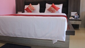A large bed with white bedding and red decorative pillows, a wooden headboard, and a bedside table with a tray of breakfast items. - Hotel Galaxy International (Puri)