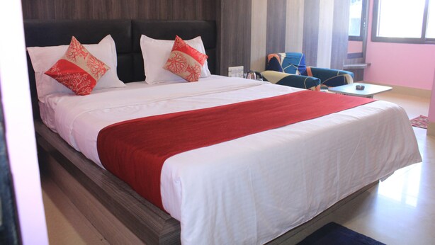 A large bed with white and red bedding, a dark headboard, and two decorative pillows. - Hotel Galaxy International (Puri)