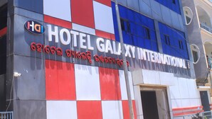 A hotel with a checkered facade, a prominent sign reading "HOTEL GALAXY INTERNATIONAL," and a parked scooter in front. - Hotel Galaxy International (Puri)