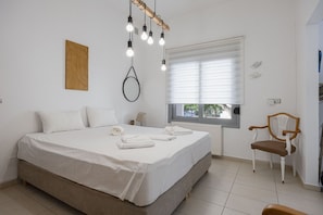 A bedroom with a bed, a chair, a window with blinds, and a wall-mounted light fixture. - Urban Brown by Domisi with private Jacuzzi (Rethymno)