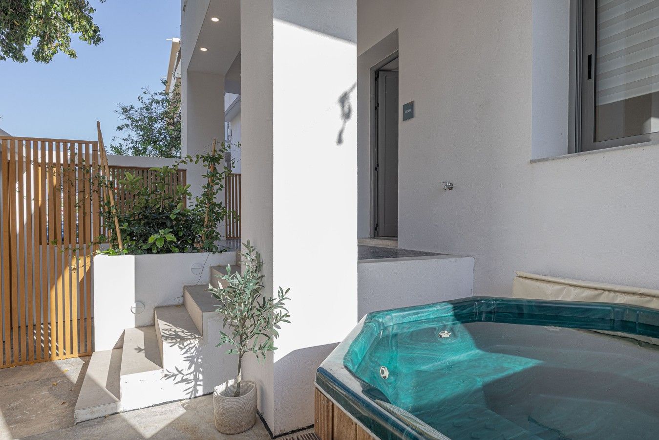 Ein moderner Poolbereich im Freien mit einem Whirlpool, einem Holenzaun und Kübelpflanzen.