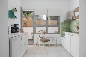 Une cuisine moderne avec des meubles blancs, une machine à café et une fenêtre donnant sur une clôture en bois.