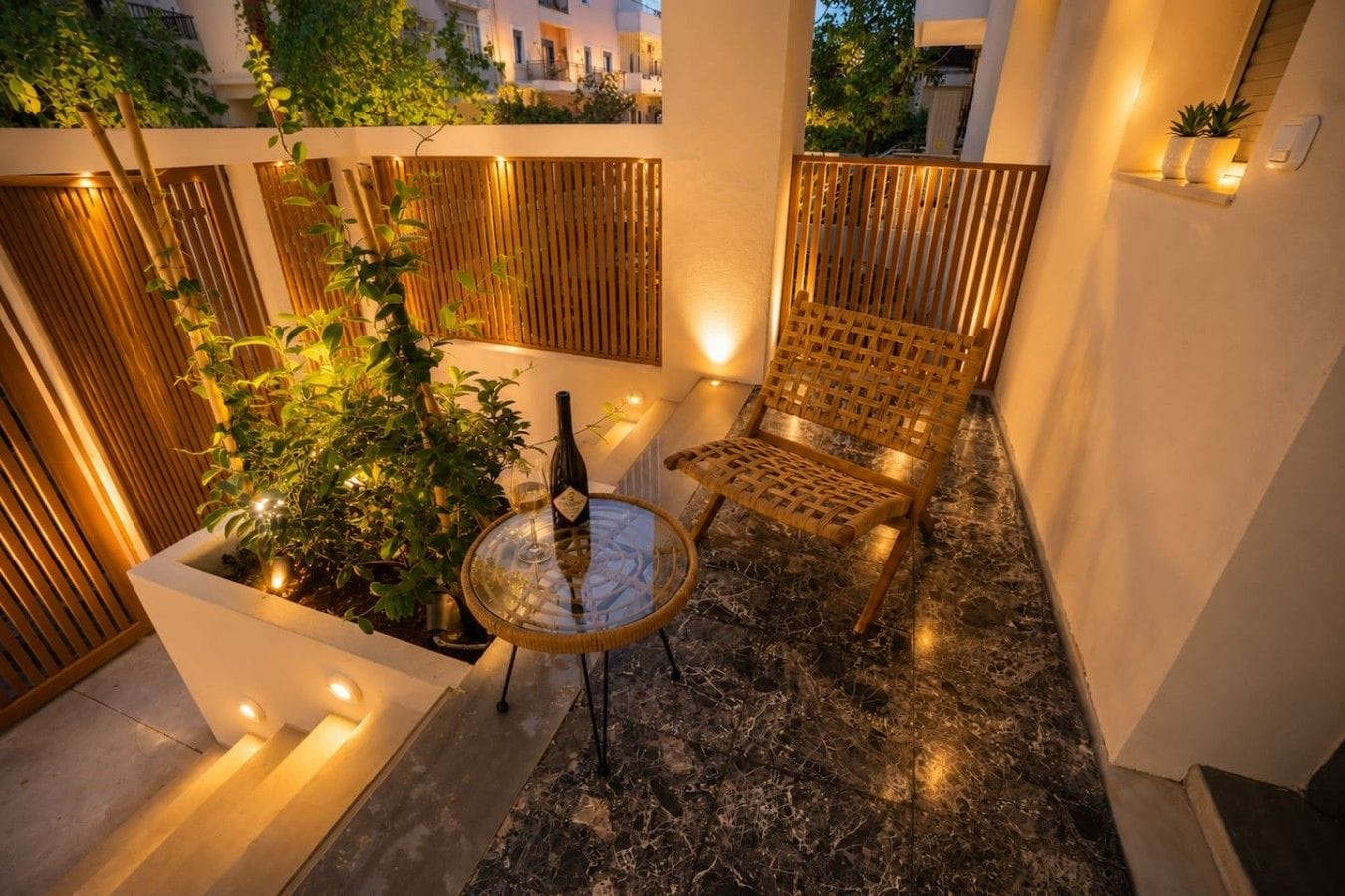 A cozy outdoor seating area with a wicker chair and a table, surrounded by plants and a wooden fence.