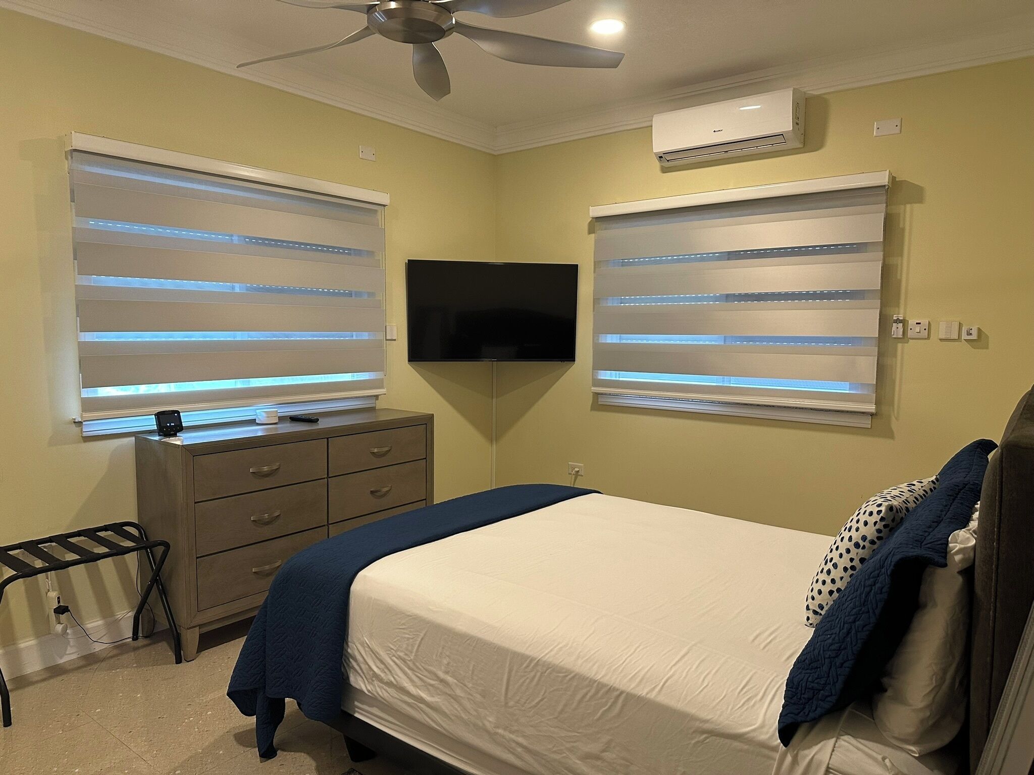 A bedroom with a bed, a dresser, a TV, and an air conditioning unit.