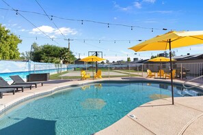 A swimming pool with lounge chairs and yellow umbrellas, surrounded by a fence and trees.