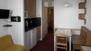A compact kitchen with wooden cabinets, a microwave, and a small dining area with a table and chairs. - Ski-in/ski-out & foot of the slopes, 2nd floor, view ski slopes, balcony, tv, ski locker, 27m² (La Plagne)