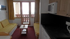A compact room with a sofa, a small table, a microwave, and a kitchenette. - Ski-in/ski-out & foot of the slopes, 2nd floor, view ski slopes, balcony, tv, ski locker, 27m² (La Plagne)