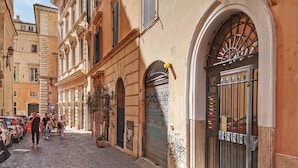 Una calle adoquinada con edificios históricos, una tienda cerrada con persianas metálicas y una planta en maceta.