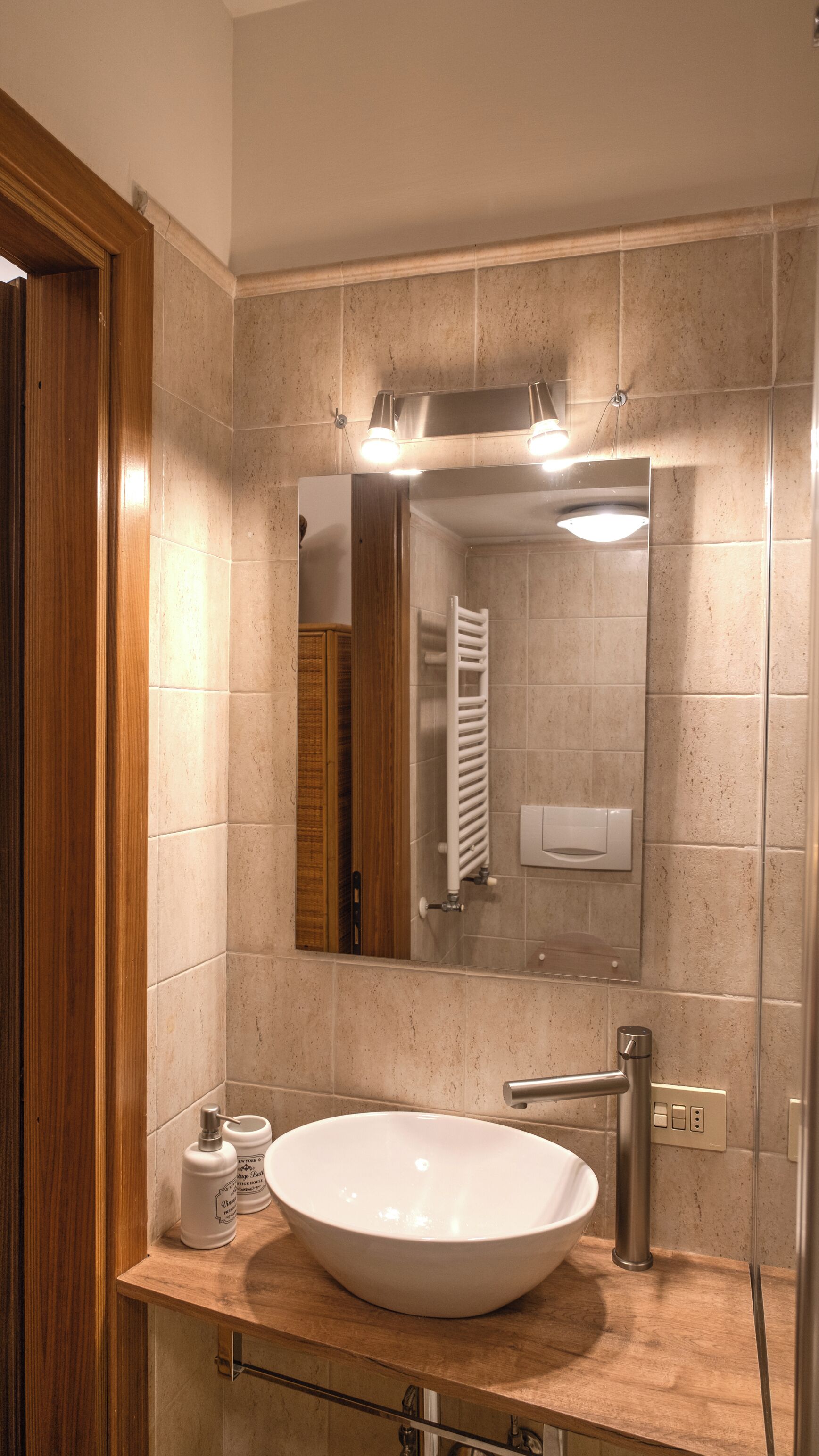 Ein Badezimmer mit einem großen Spiegel, einem weißen Waschbecken, einem Handtuchhalter und einem Holzlagerplatz.