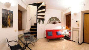 Una sala de estar moderna con una mesa de vidrio, un sofá rojo, una escalera en espiral y un ventilador en la pared.