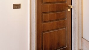 Una puerta de madera con picaporte de latón y cerradura, sobre una pared blanca con zócalo de mármol.
