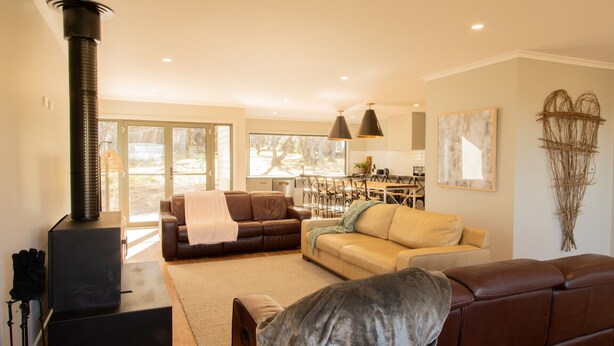A living room with a fireplace, two sofas, a coffee table, and a dining area in the background. - The Staggerinn - Dinner Plain (Dinner Plain)