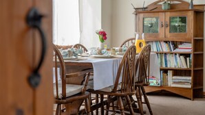 A dining area with a wooden table set for four, surrounded by wooden chairs. A bookshelf filled with books is to the right. - Higher Gills Farm, Stunning Views, 4 bedroom (Clitheroe)