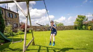A child playing on a swing set in a backyard with a stone wall, a slide, and a building in the background. - Higher Gills Farm, Stunning Views, 4 bedroom (Clitheroe)