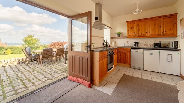 A kitchen with wooden cabinets, a built-in oven, and a view of a garden through a sliding glass door. - Higher Gills Farm, Stunning Views, 4 bedroom (Clitheroe)