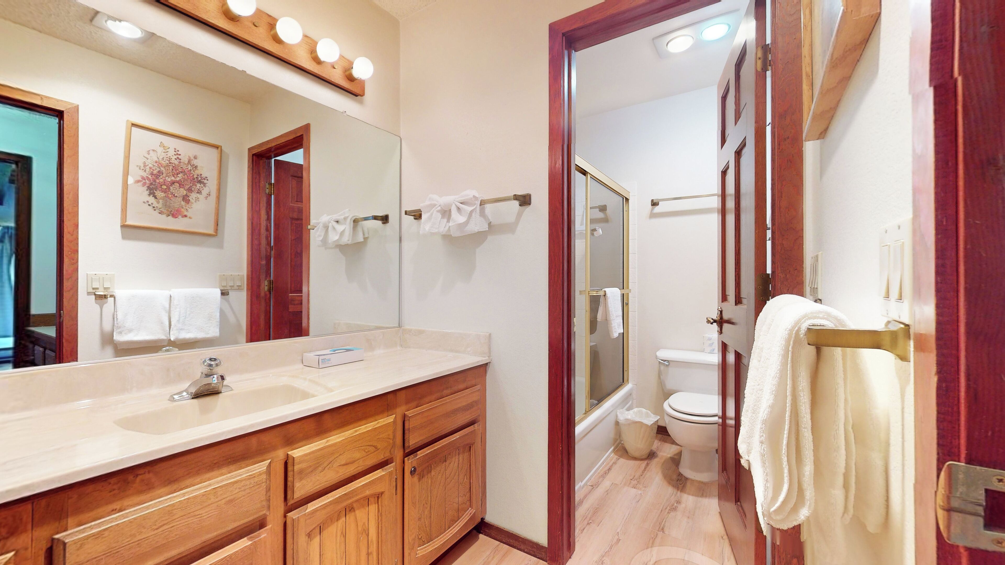 A bathroom with a large mirror, wooden cabinets, a sink, and a shower area.