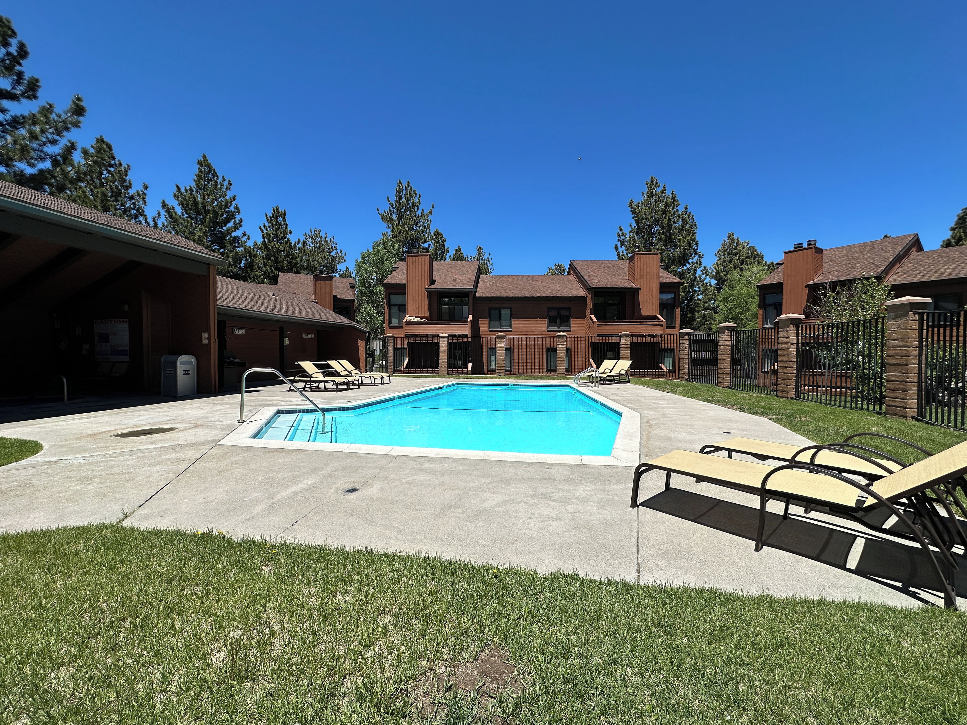 A swimming pool with lounge chairs, a covered area, and a brick building with multiple windows.