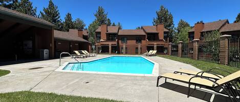 A swimming pool with lounge chairs, a covered area, and a brick building with multiple windows.