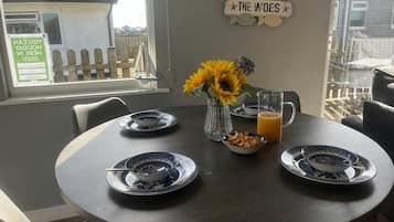 Een eettafel gedekt met borden, een vaas met zonnebloemen, een kom cornflakes en een glas sinaasappelsap.
