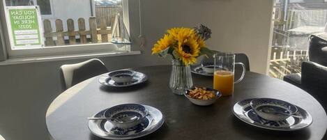 A dining table set with plates, a vase with sunflowers, a bowl of cereal, and a glass of orange juice.