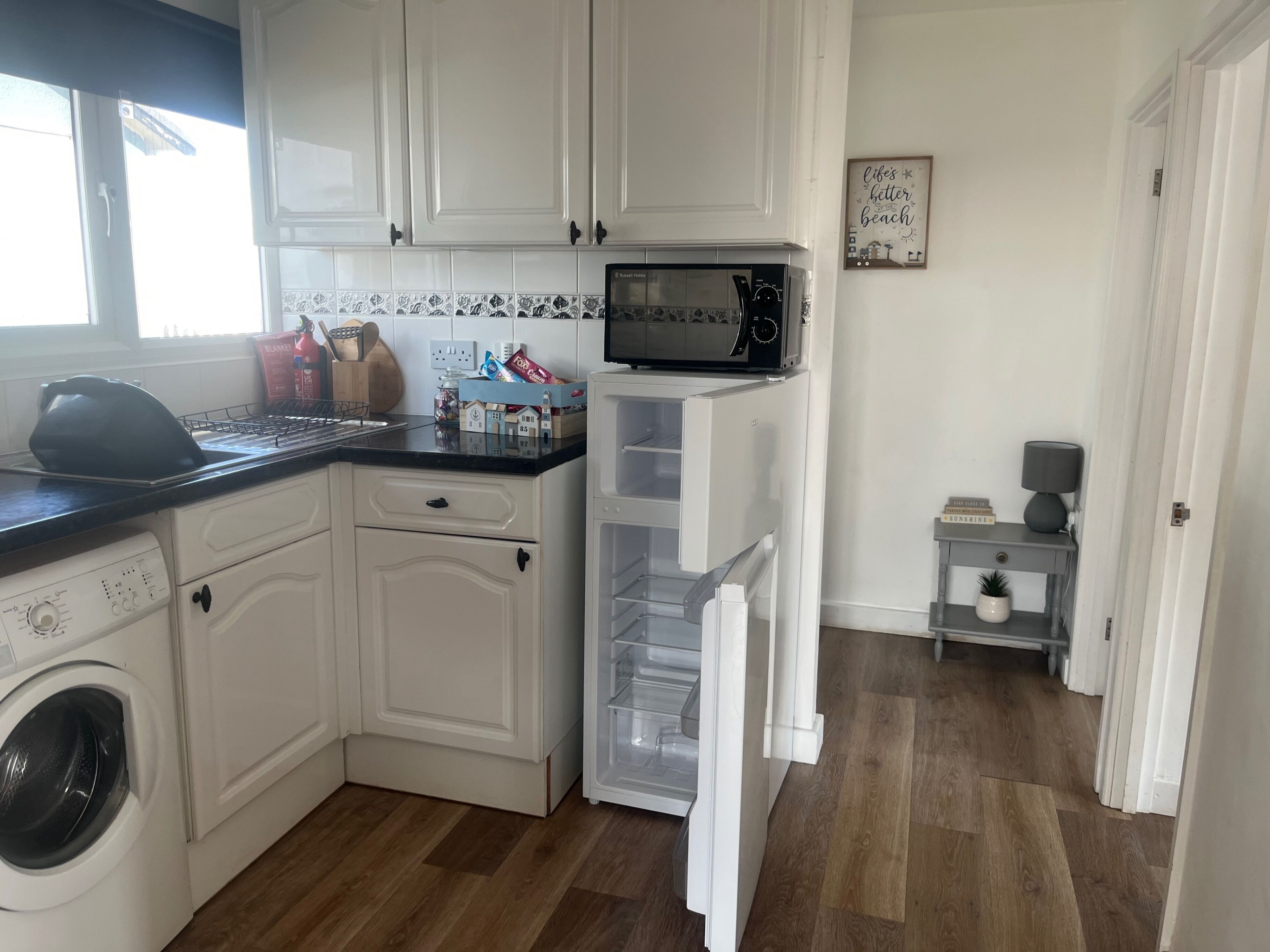 Une cuisine compacte avec des meubles blancs, un four à micro-ondes, un lave-vaisselle encastré et un lave-linge.