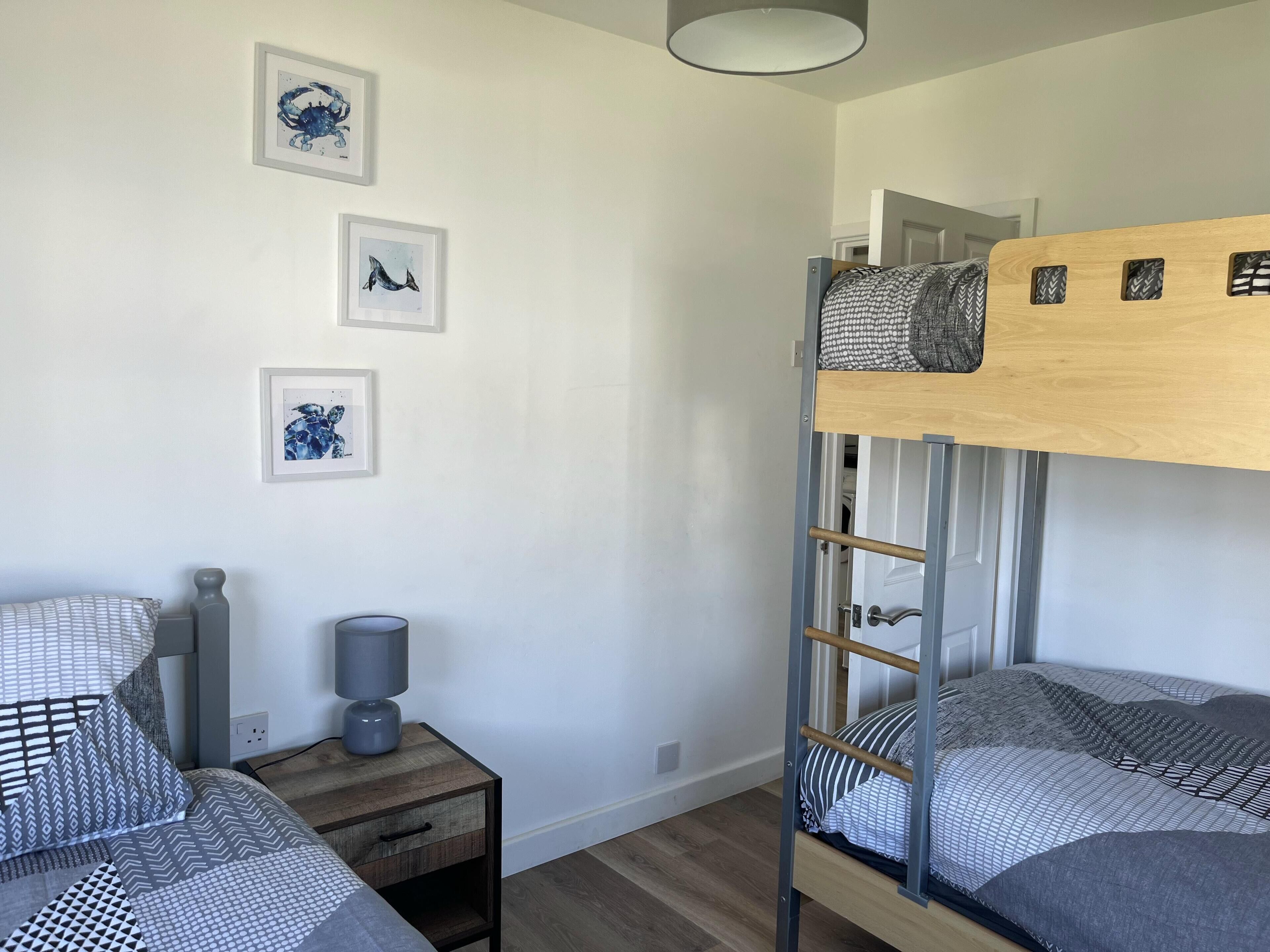 A bunk bed room with a wooden headboard, a bedside table with a lamp, and three framed pictures on the wall.