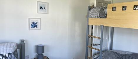 A bunk bed room with a wooden headboard, a bedside table with a lamp, and three framed pictures on the wall.