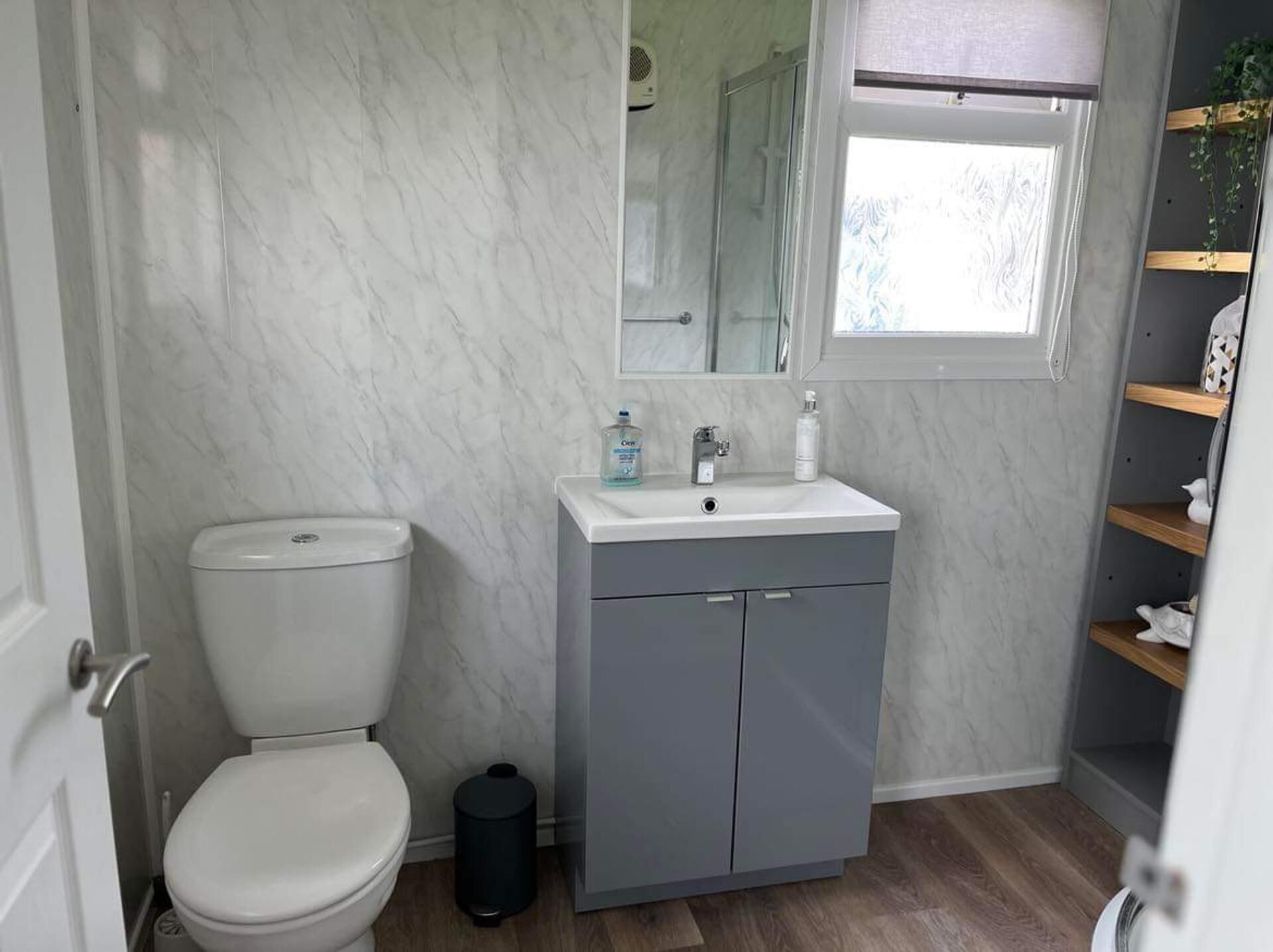 Et badeværelse med toilet, vask og et spejl over vasken, samt et vindue.
