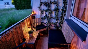 Un balcon doté de meubles en bois, d’une plante en pot et offrant une vue sur la verdure.