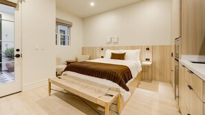 Un dormitorio moderno con una cama grande, mesitas de noche, un banco y vistas al exterior.