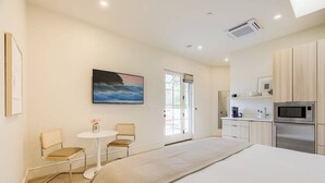 Une chambre d’hôtel moderne avec un grand lit, une petite table ronde, deux chaises, un coin cuisine équipé d’un four à micro-ondes et d’un réfrigérateur, et un tableau accroché au mur.