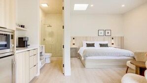 Habitación de hotel moderna con kitchenette, una cama grande, una mesita de noche y zona de ducha.