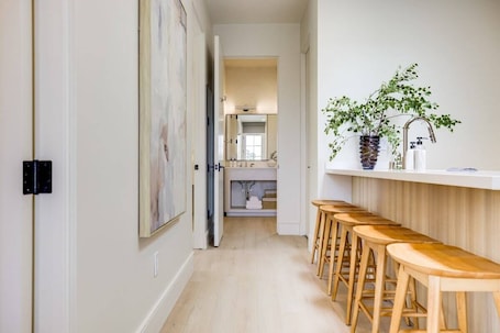 A hallway with wooden stools, a sink, and a mirror.