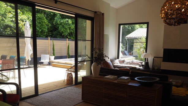 A modern living room with a large sliding glass door leading to a patio area. - Chambre D'hôtes En Apar-té en Fond de Jardin Calme Relaxation Piscine (Toulouse)