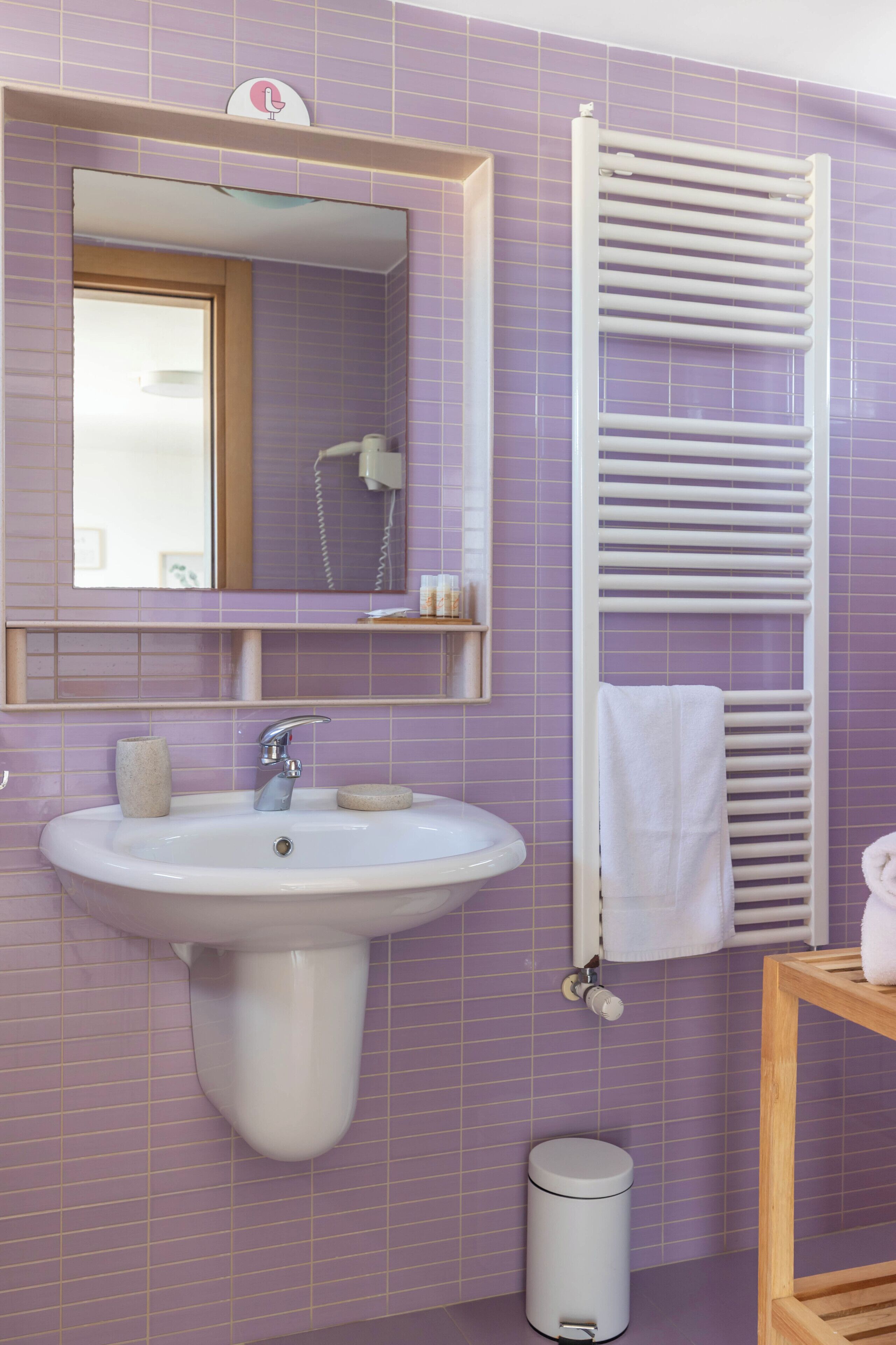 A bathroom with a sink, mirror, towel rack, and waste bin.