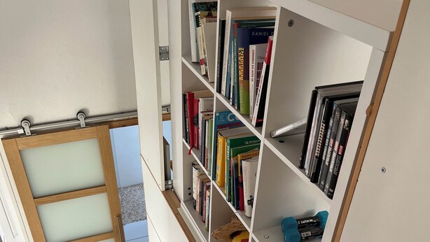 A staircase with a wooden handrail leading to a white bookshelf filled with books and DVDs. - Bright and friendly bungalow in a naturist beach vacation village in Corsica (Linguizzetta)