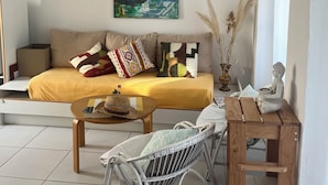 A modern living room with a sofa, a coffee table, and a chair. There is a painting on the wall and a statue on a small table. - Bright and friendly bungalow in a naturist beach vacation village in Corsica (Linguizzetta)