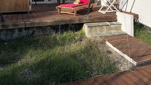 A wooden deck with a red lounge chair, a wooden bench, and a table. - Bright and friendly bungalow in a naturist beach vacation village in Corsica (Linguizzetta)