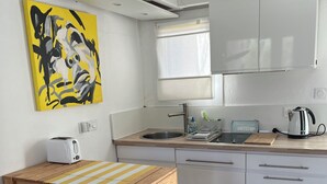 A compact kitchen with white cabinets, a stainless steel sink, a toaster, a kettle, and a wooden table with a stool. - Bright and friendly bungalow in a naturist beach vacation village in Corsica (Linguizzetta)
