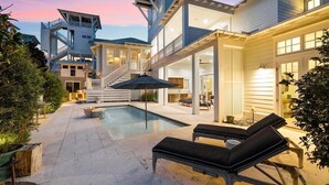 Une maison moderne dotée d’une piscine, d’un espace salon extérieur et d’un escalier menant à un étage supérieur.