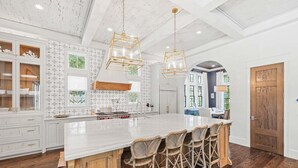 Une cuisine spacieuse dotée d’un grand îlot central, de meubles blancs et d’un plafond en bois.