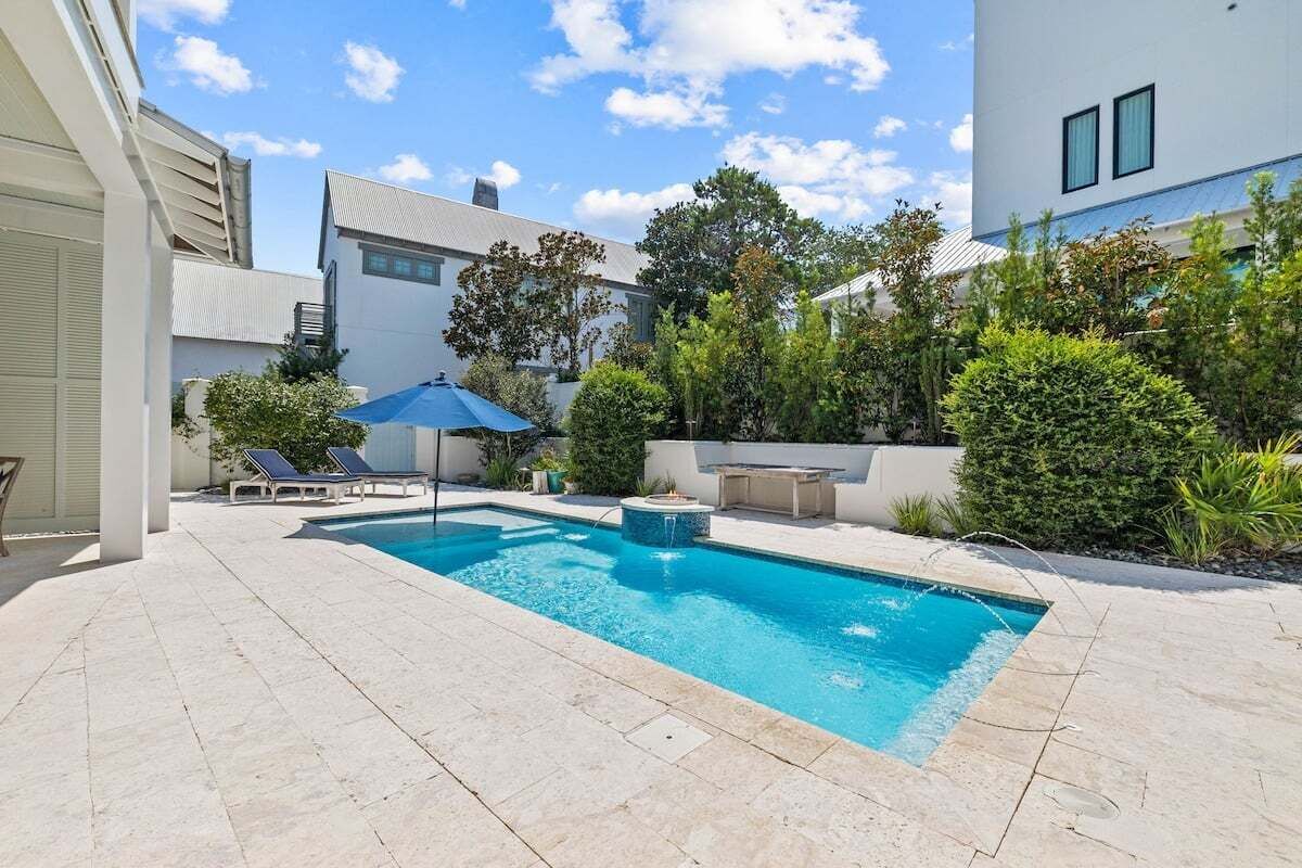 A swimming pool with lounge chairs and a hot tub, surrounded by greenery and modern buildings.