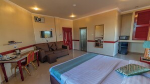 Una habitación de hotel con una cama grande, un sofá, un escritorio con una silla, un televisor y un espejo.